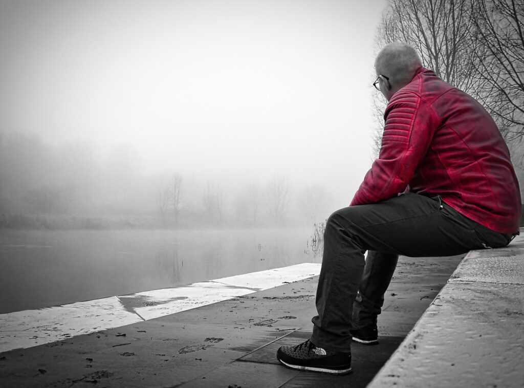 A self-portrait of the author by a river with his gaze turned away from the viewer. The colors are completely desaturated, except for the red leather jacket. 
