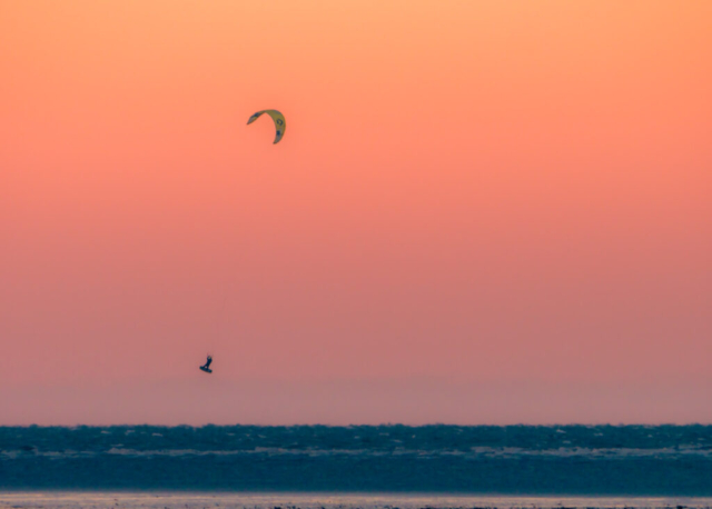 Ein Kitesurfer springt vor dem orangefarbenen Abendhimmel