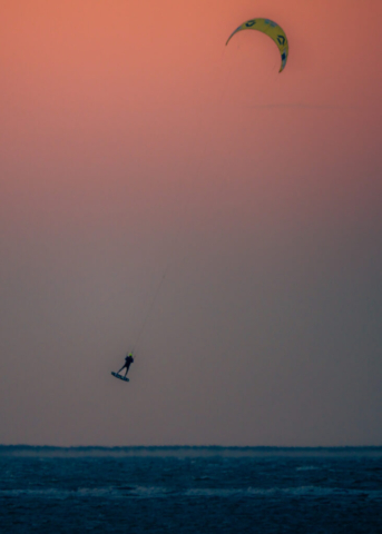 Ein Kitesurfer springt vor dem orangefarbenen Abendhimmel