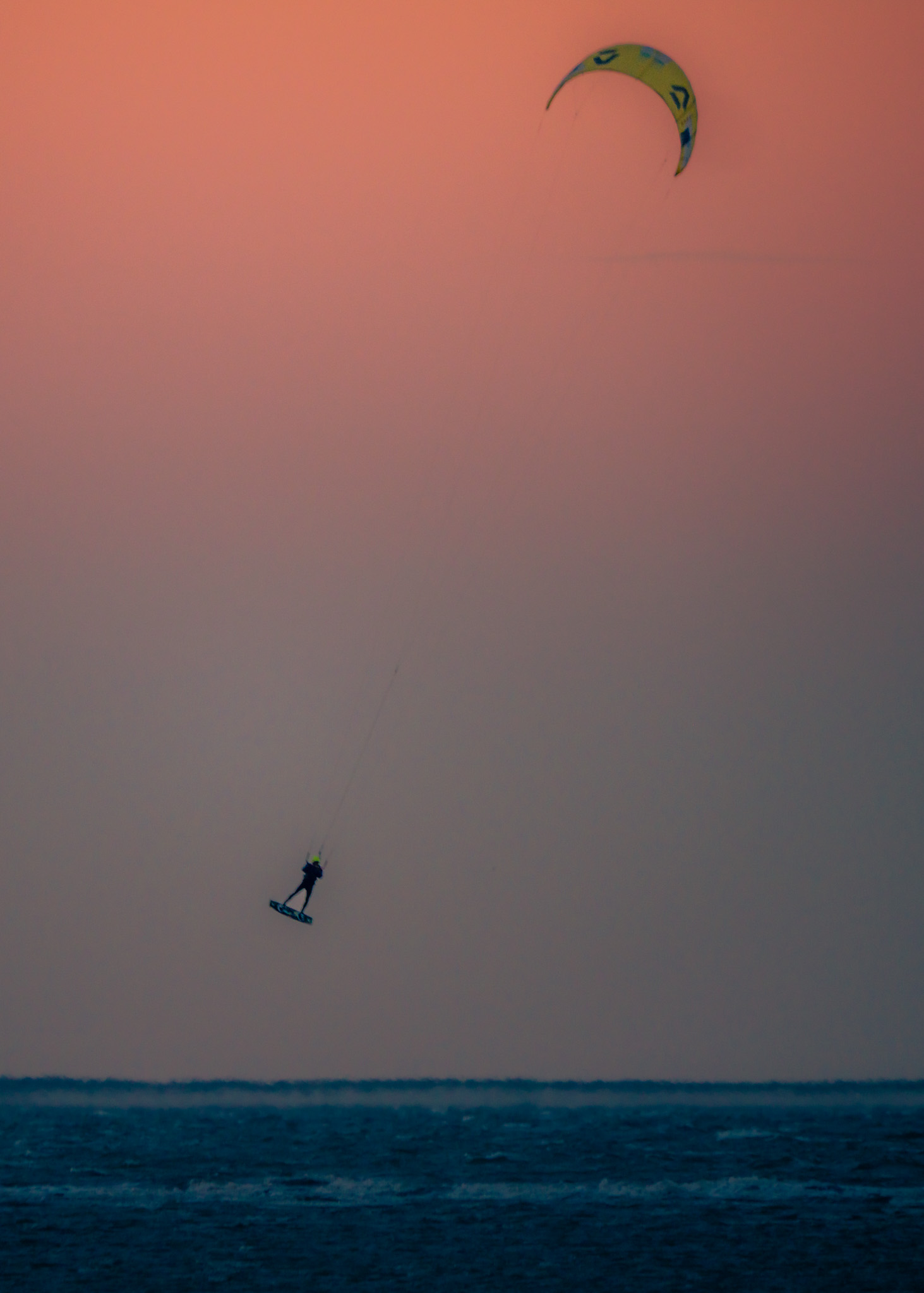 Ein Kitesurfer springt vor dem orangefarbenen Abendhimmel